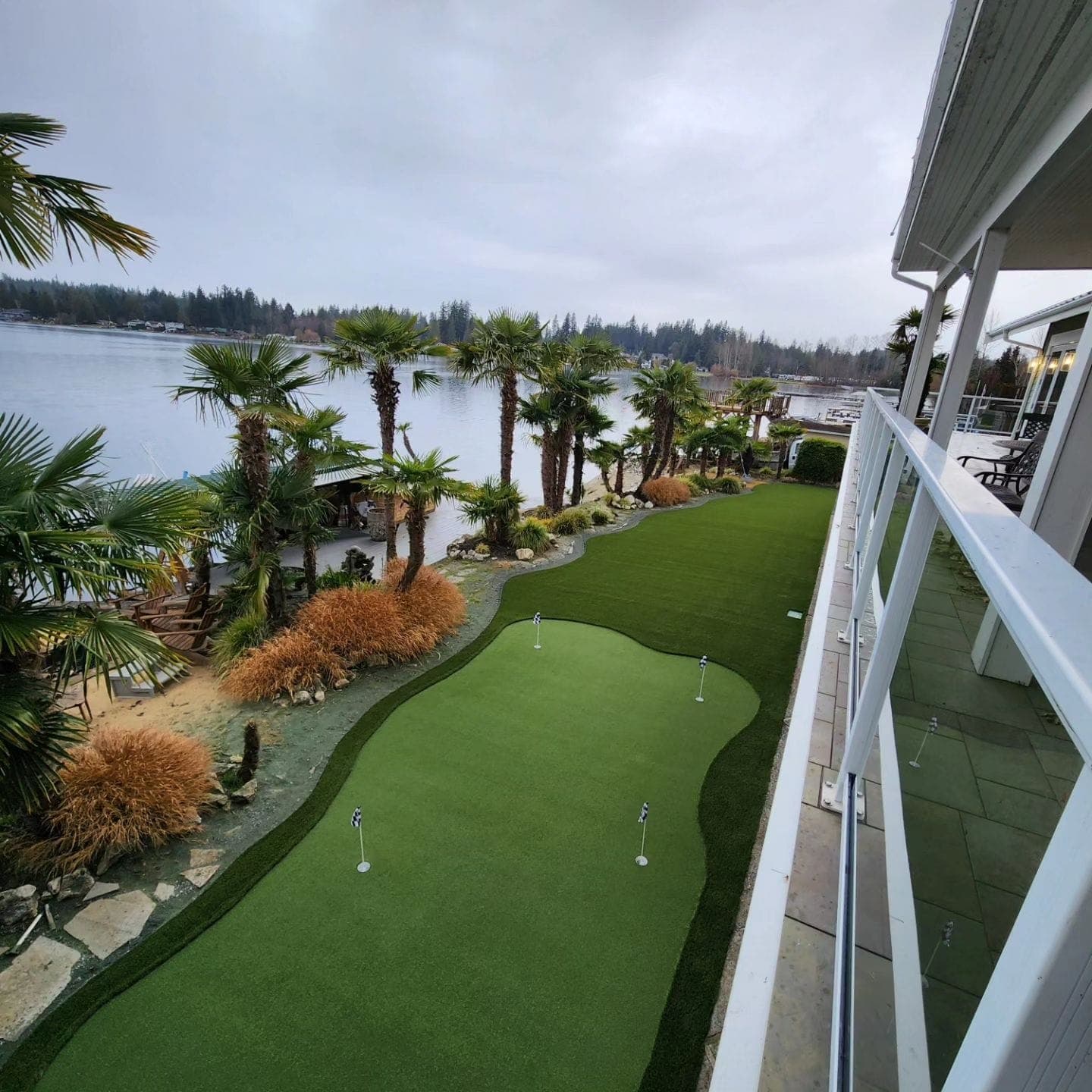 Custom multi-hole backyard putting green overlooking a lake, lined with palm trees