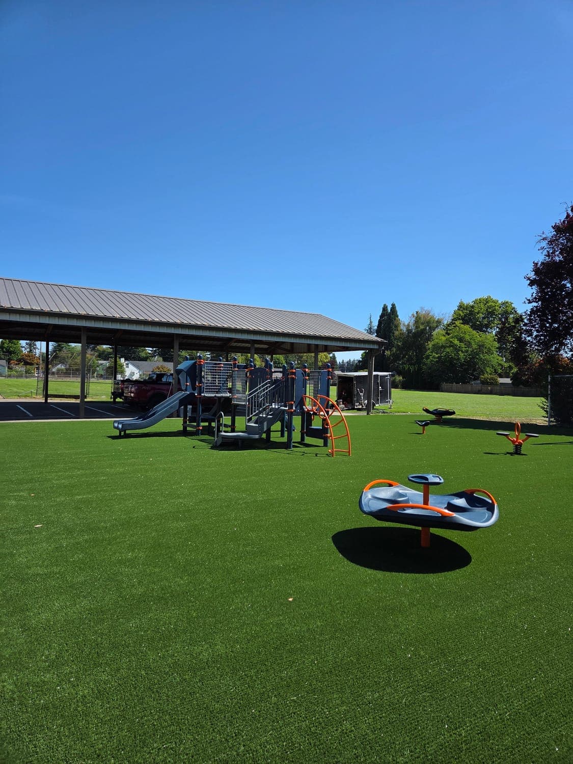 Park playground with an open artificial turf field and a shade structure