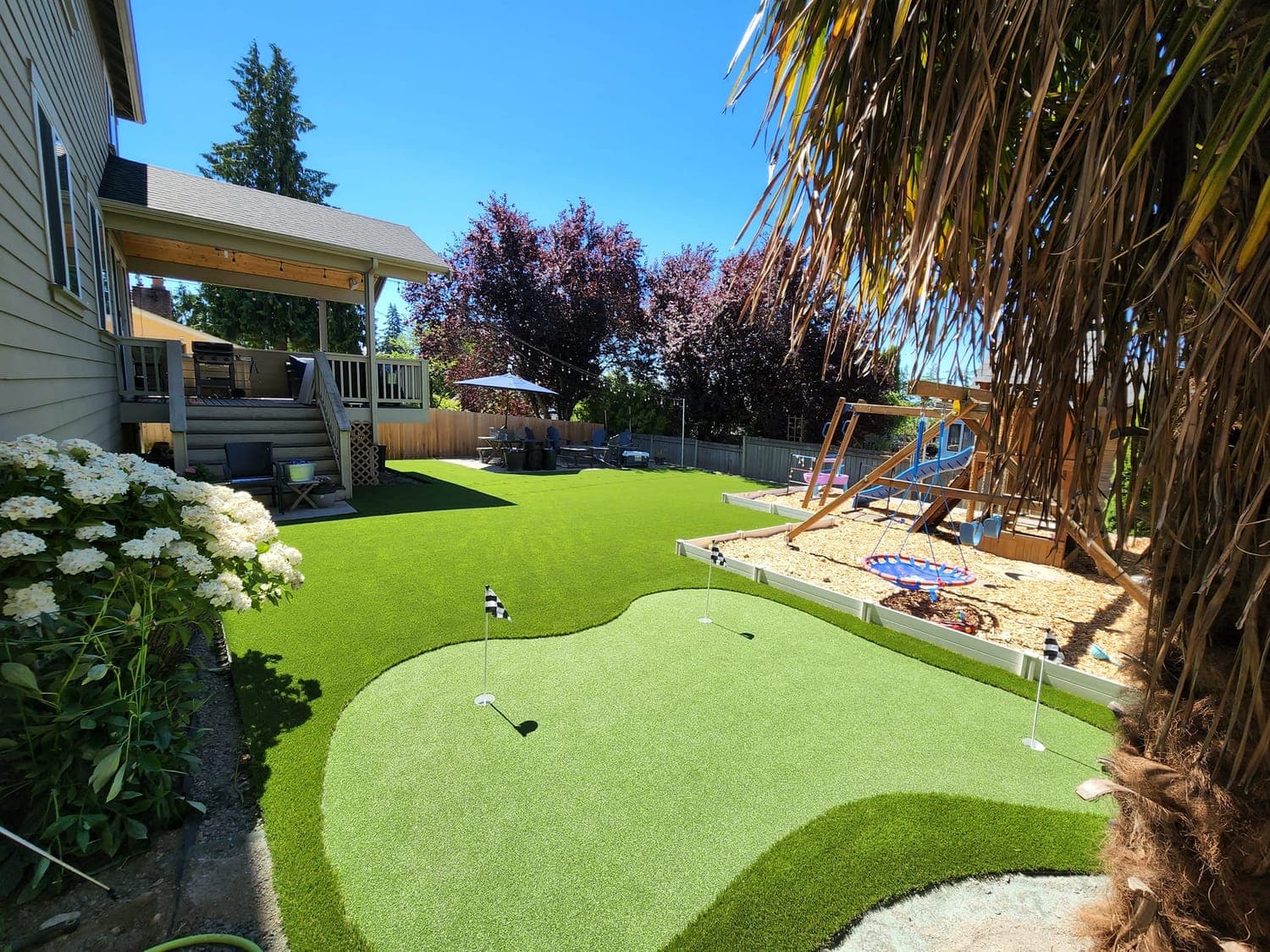 Backyard putting green with cups and a playset showing a smooth synthetic putting surface
