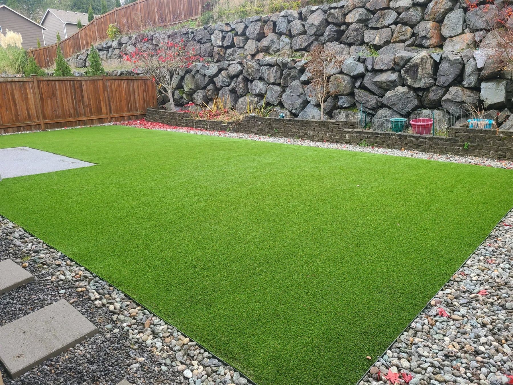 Fresh artificial lawn bordered by a retaining wall and landscaping