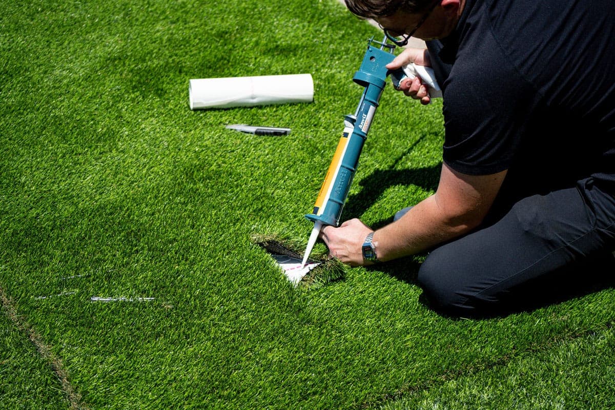 Synthetic Turf Solutions installer applying adhesive and seaming artificial turf during a repair
