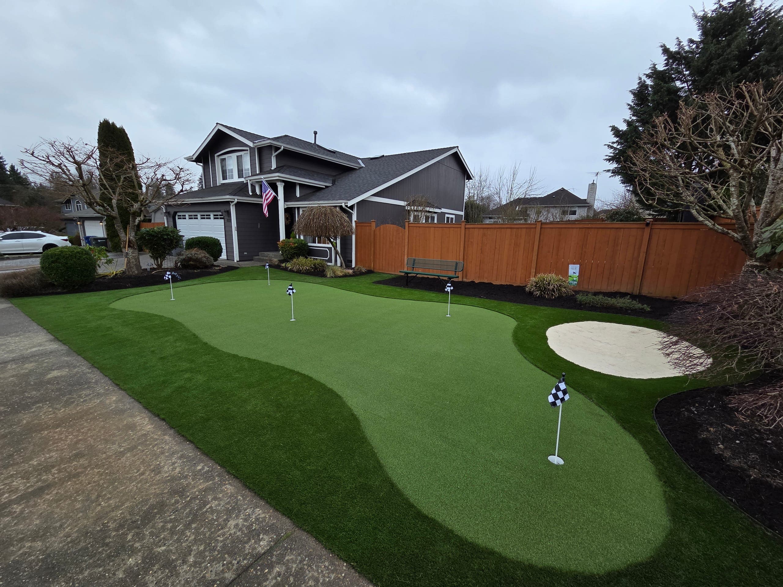 Front-yard putting green with practice flags and a sand bunker installed by Synthetic Turf Solutions